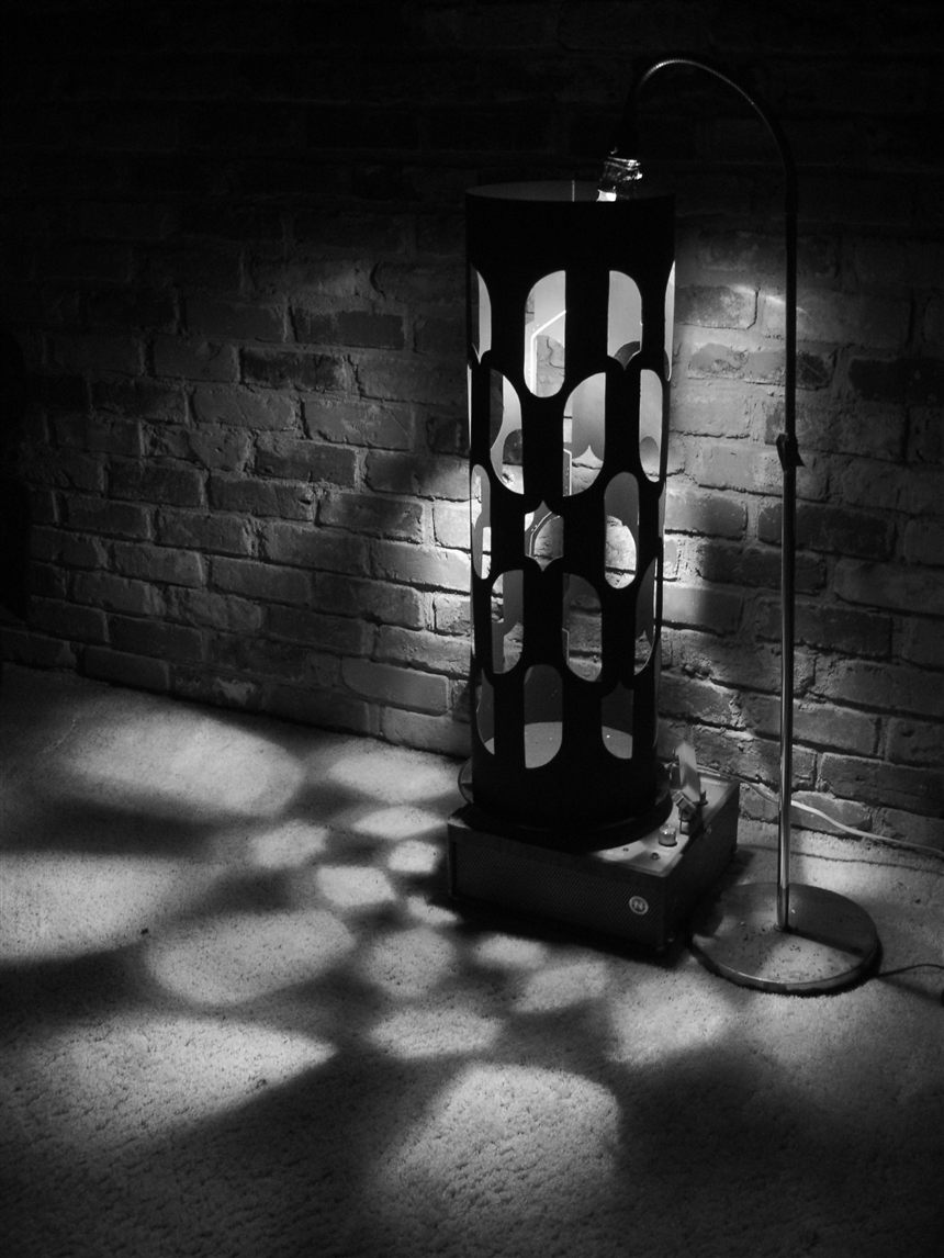 Black-and-white photograph of a homemade Dreamachine: a slotted cylinder on a turntable in a dark room